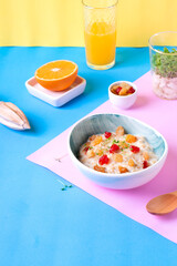 Porridge with milk, dried cherry and raisin in ceramic bowl and fresh orange juice against the colorful background. Breakfast meal