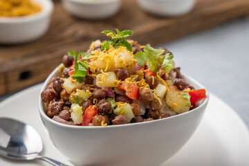 black gram or kala chana chaat with boiled potato, onion, tomato with a dash of lemon juice served on a white bowl