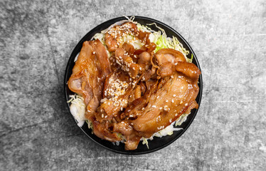 Rice topped grilled sliced pork belly with soy sauce and sesame seed on the concrete table..