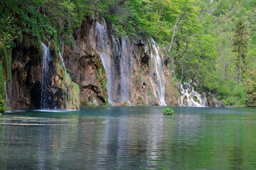 Fototapeta na wymiar Plitvice lakes national park in Croatia, beautiful emerald color water in lake, with reflections, waterfalls, hill with green, trees, bushes