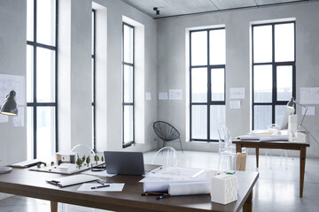 Image of light modern office with table with carton model of new building and blueprints on it
