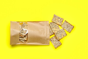 Tasty crackers with seeds in bag on color background