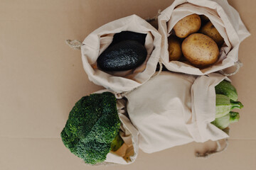 Reusable storage bags for vegetables and fruits on cardboard background. Storage bags with potatoes, lettuce, avocado, zucchini, broccoli. Healthy food in storage bags.