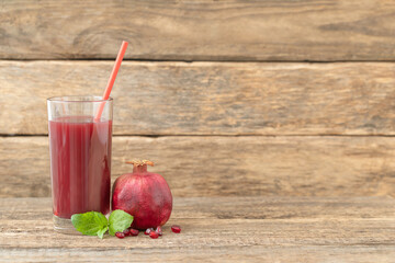 A glass of pomegranate juice, a whole pomegranate and a mint leaf on a wooden background