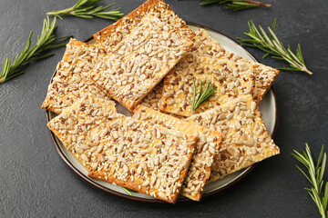 Tasty crackers with seeds in plate on dark background
