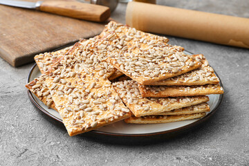 Tasty crackers with seeds in plate on grey background