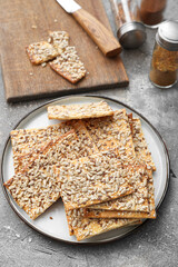 Tasty crackers with seeds in plate on grey background