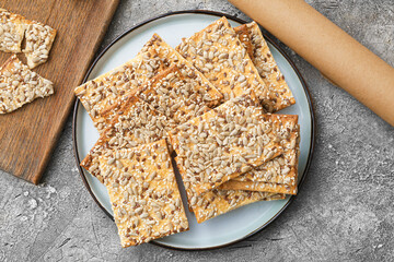 Tasty crackers with seeds in plate on grey background