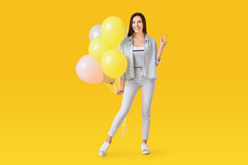 Beautiful young woman with balloons showing victory gesture on color background