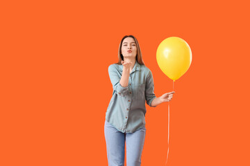 Beautiful young woman with balloon blowing kiss on color background