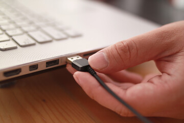 Close up of hand inserting plugging data cable into usb port in laptop, data transfer