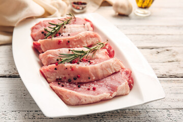 Plate with fresh raw meat and spices on light wooden background