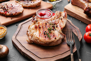 Board with tasty steak and spices on dark background