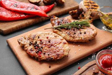 Board with tasty steaks and spices on dark background