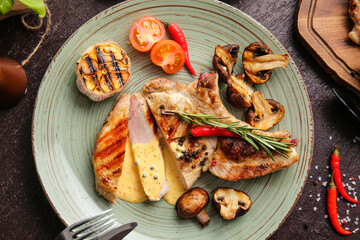Plate with tasty steaks and spices on dark background