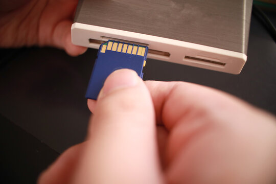 Close up of person hand inserting sd card memory into card reader, data transfer