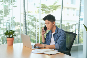  man talking on mobile phone, working from home. Portrait of pensive asian businessman using laptop computer, planning project, communication in modern office