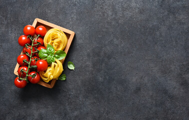 Ingredients for the pasta. Tagliatelle pasta, tomatoes and basil on a black concrete background.