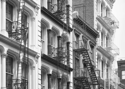 Row of old buildings with iron fire escapes, black and white picture, New York City, USA.