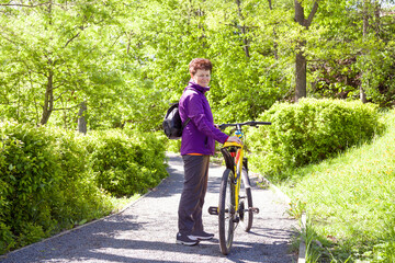 Portrait of happy adorable senior woman riding a bike in summer park