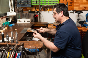 goldsmith jeweler polishes and sands a silver ring with a metal file