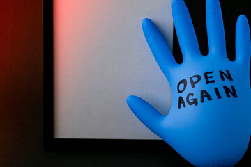 Blown up blue latex surgical glove on black background. Reopening covid safe. Open again text...