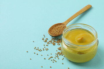 Jar with mustard and spoon with seeds on blue background