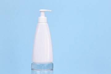 Unbranded white pump cream or liquid soap bottle on glass podium on blue background. Cosmetic packaging mockup with copy space. Template, front view.