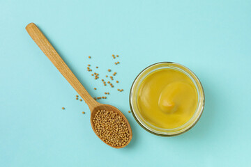 Jar with mustard and spoon with seeds on blue background