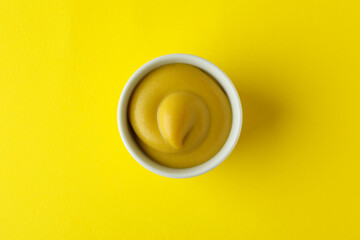 Bowl with mustard on yellow background, top view