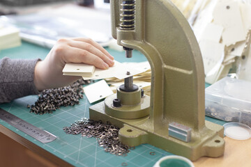 close-up man hands insert grommets and eyelet into clothing tags on a large manual press...