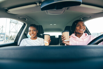 Two african woman drinkink coffee to go in the car while driving car on the road
