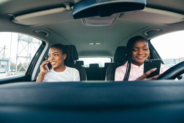 Two african woman use phones in the car while driving car on the street road
