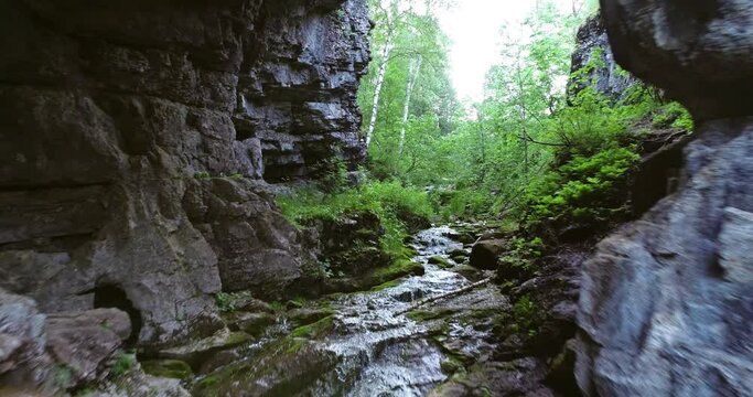 Mountain creek with cascade waterfall and rocky arch in wild nature reserve in Ural Mountains. Aerial drone wide shot at summer day.
