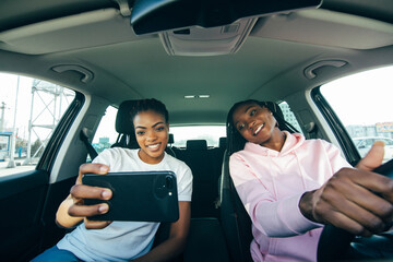 Smiling african woman taking selfie with smart phone in the car. Vacation, holidays, tourism and modern technology concept.