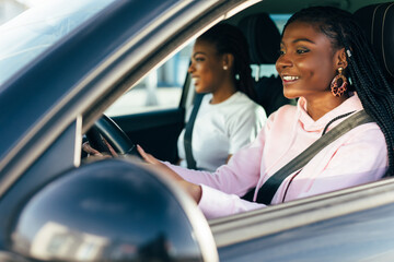 Perfect start of holidays. Two beautiful african young cheerful women looking at each other with smile while sitting in car