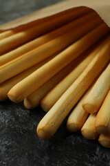 Paper bag with grissini breadsticks on black smoky background