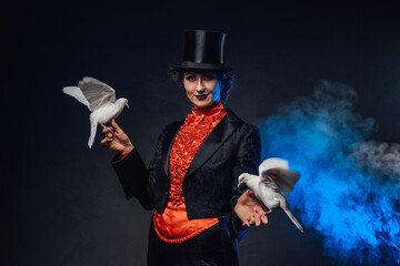 Mysterious circus actress holding two little doves on her hands in smoke