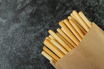 Paper bag with grissini breadsticks on black smoky background
