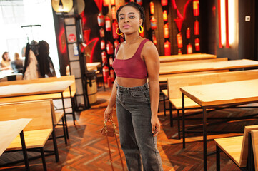 African woman in red marsala top and jeans posed indoor.
