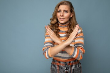 Photo of young attractive upset angry dissatisfied blonde woman with sincere emotions wearing striped sweater isolated over blue background with copy space and showing no gesture and stop sign with