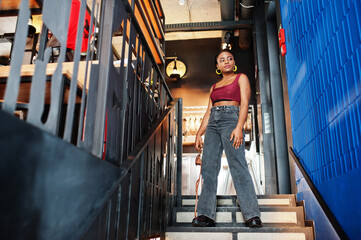 African woman in red marsala top and jeans posed indoor.