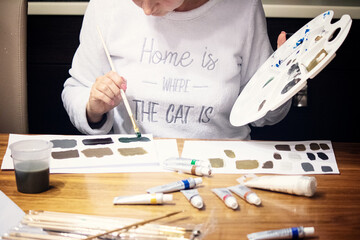 Pretty woman painting with brush and acrylic paints in artistic studio. Pensive female standing at easel with colorful picture.
