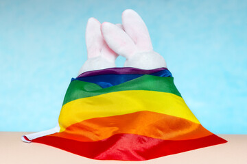 Cute couple of pink stuffed bunny hugging rolled up in rainbow lgbtq flag, shoot from back, LGBTQIA culture concept