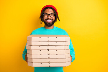 Portrait of brunette optimistic guy hold pizza wear cap spectacles blue pullover isolated on yellow vivid color background