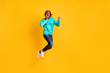 Fototapeta na wymiar Full size profile photo of brunette optimistic guy jump point empty space wear cap spectacles pullover jeans isolated on yellow background