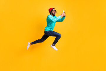 Fototapeta na wymiar Full size profile photo of brunette optimistic guy jump run take photo wear cap spectacles pullover jeans isolated on yellow background