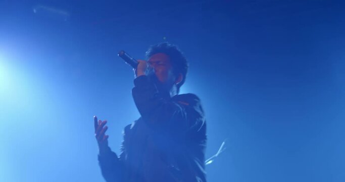 Asian vocal rock star band musician performing in stage in night club with spotlight and colorful laser ray. Singer playing to the crowd audience on music festival indoor concert