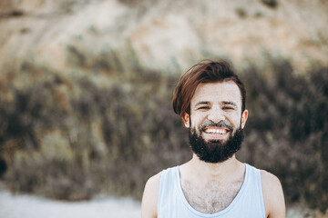 Naklejka na ściany i meble portrait of a stylish young man with a beard and a face on which the sea sand on the background of the sea shore