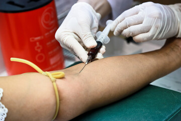 Doctor or nurse hands in medical white gloves using needle syringe drawing blood sample from patient arm in hospital.